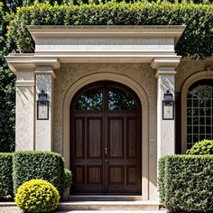 the front entrance to a house with two large wooden doors and trimmed hedges on either side