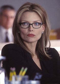 a woman wearing glasses sitting at a table with pens and pencils in front of her