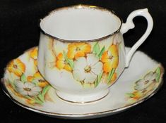 a tea cup and saucer with flowers painted on the side sitting on a black surface