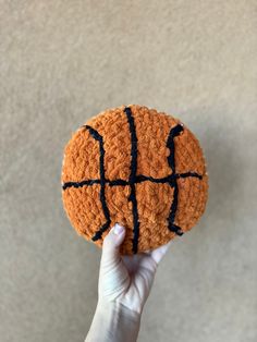 a hand holding an orange crocheted basketball ball with black stitching on it