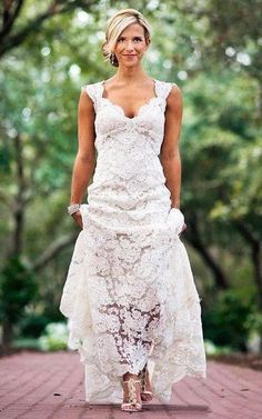 a woman in a white dress is standing on a brick path with trees behind her