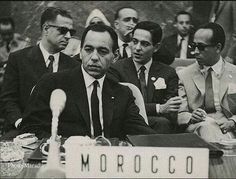 black and white photograph of men sitting at a table with microphones in front of them