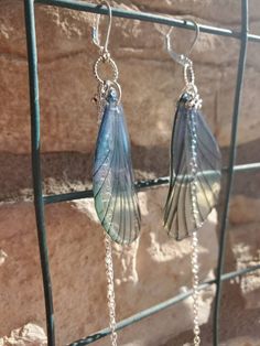 two earrings hanging from a metal rack next to a stone wall with chains attached to it