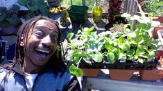 a man with dreadlocks standing in front of some plants and smiling at the camera