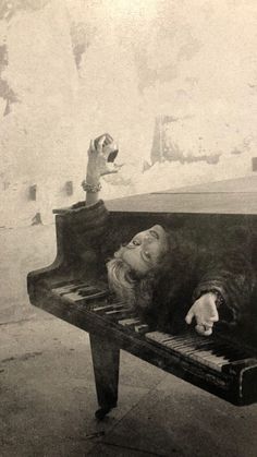 an old black and white photo of a woman laying on a piano