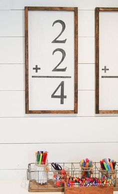 two framed numbers are on the wall next to some pens and pencils in baskets