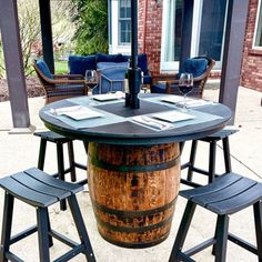 a wooden barrel table with four stools and a wine glass on it in front of a brick house