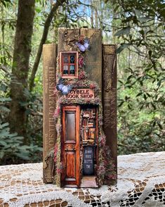 an altered book is sitting on top of a doily covered tablecloth in the woods