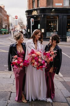 three bridesmaids standing on the sidewalk with their bouquets in hand and one woman wearing a long white dress