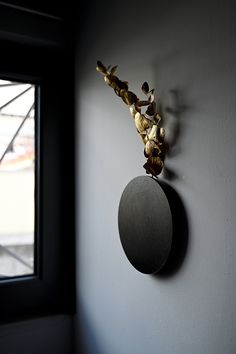 a clock mounted to the side of a wall next to a window with a plant growing out of it