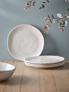 three white plates sitting on top of a wooden table next to a vase with flowers