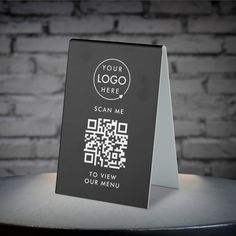 a black and white sign with qr code on it sitting on a table next to a brick wall