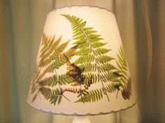 a lamp with a green fern print on the shade is sitting on a table next to a window