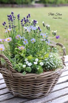 a basket filled with lots of flowers sitting on top of a wooden table next to grass