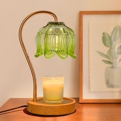 a green glass lamp sitting on top of a wooden table next to a lit candle