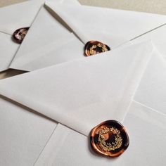 some white envelopes with gold designs on them and one has a button in the middle