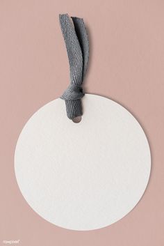 a white round tag with a gray ribbon on a light pink background that is blank