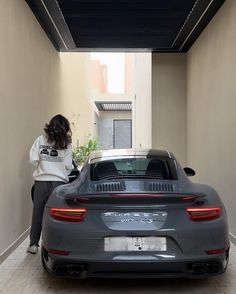 a woman standing next to a gray sports car in a narrow room with an open door