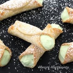 several pastries are arranged on a black surface with powdered sugar scattered around them