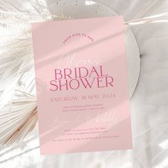 a pink and white bridal shower party card on a bed with palm fronds