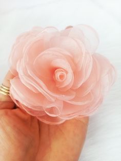 a woman's hand holding a pink flower on top of white furnishing