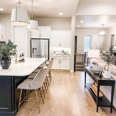 An eat-in kitchen is created with elegant gray velvet and gold chairs seated at a black kitchen island. The island is topped by a white countertop lit by white and gold pendant lamps. The island stands in front of white kitchen cabinets...   Image: ourcoloradomountainhome