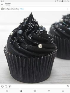 two cupcakes with black frosting and sprinkles sitting on top of each other