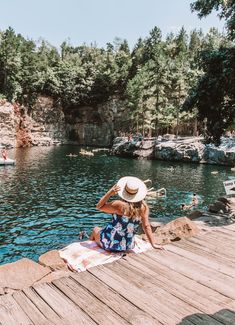 a woman in a hat sitting on a dock next to the water and looking at ducks