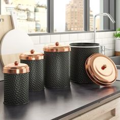 four black canisters with copper lids on a kitchen counter