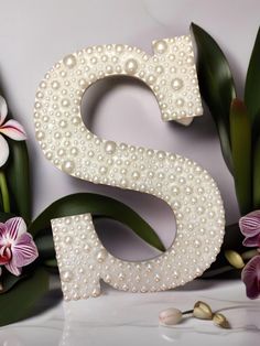 the letter s is made out of pearls and surrounded by orchids on a white surface