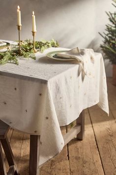 a table with two candles on it and a christmas tree in the corner behind it