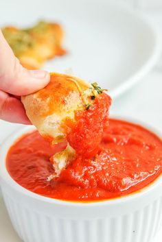 a person dipping some food into a white bowl filled with tomato sauce and bread croutons