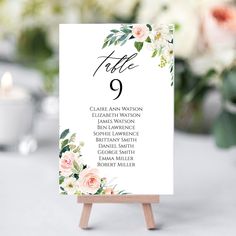 a table number card with flowers and greenery is displayed on an easel next to a candle