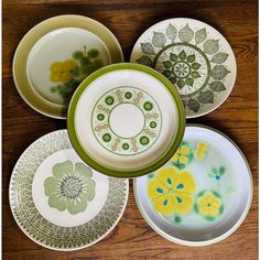 four plates with flower designs on them sitting on a wooden table next to each other