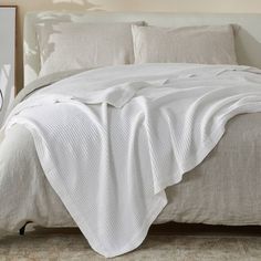 an unmade bed with white linens in a neutral colored bedroom, and a clock on the wall next to it