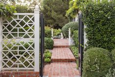 a brick path leads to a white gate with black trim and trellis on either side