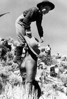 an old black and white photo of a man on a horse with people in the background