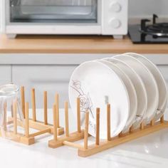 a stack of white plates sitting on top of a wooden rack in front of a microwave