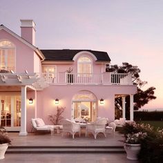 a pink house is lit up at night with white furniture and flowers in the foreground