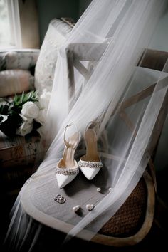 a pair of white high heel shoes sitting on top of a chair next to a veil