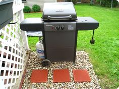 a bbq grill sitting on top of a gravel covered ground next to a white fence