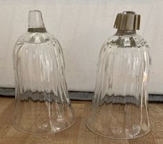 two clear glass vases sitting next to each other on a wooden floor near a white wall