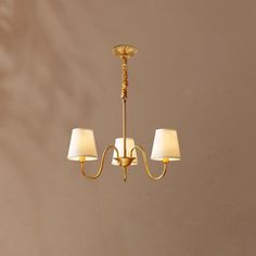 a gold chandelier with three lamps hanging from it's sides and two white shades