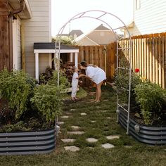 a woman and child are in the yard with some plants on each side of the fence