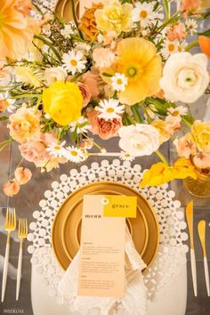 a place setting with yellow and white flowers in the center, along with an empty menu card