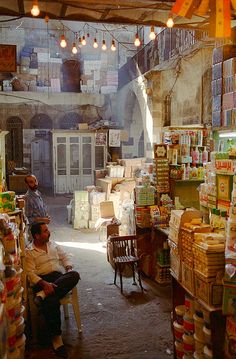 two men are sitting in the middle of a store filled with food and goods,