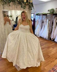 a woman in a white dress is laughing while standing in front of some wedding gowns