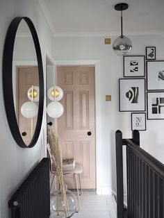 a hallway with pictures on the wall and a large round mirror hanging over it's railing