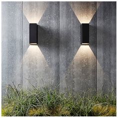 two outdoor lights are on the side of a building with grass growing in front of it