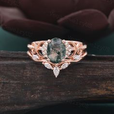 a ring with a green stone and white diamonds on the side, sitting on top of a piece of wood